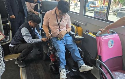 저상버스 운전기사가 휠체어에 좌석 고정벨트를 채우고 있는 장면